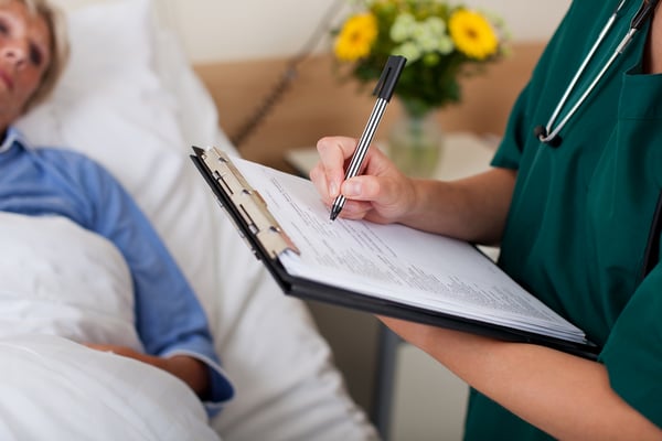 Writing on clipboard with patient in background in hospital